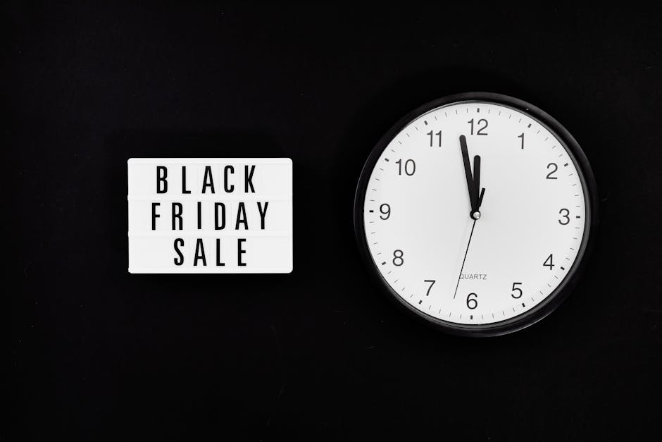 A close-up image showing a white rectangular sign with black text reading 'BLACK FRIDAY SALE' positioned on a black background, placed next to a round white clock with black hour and minute hands, and